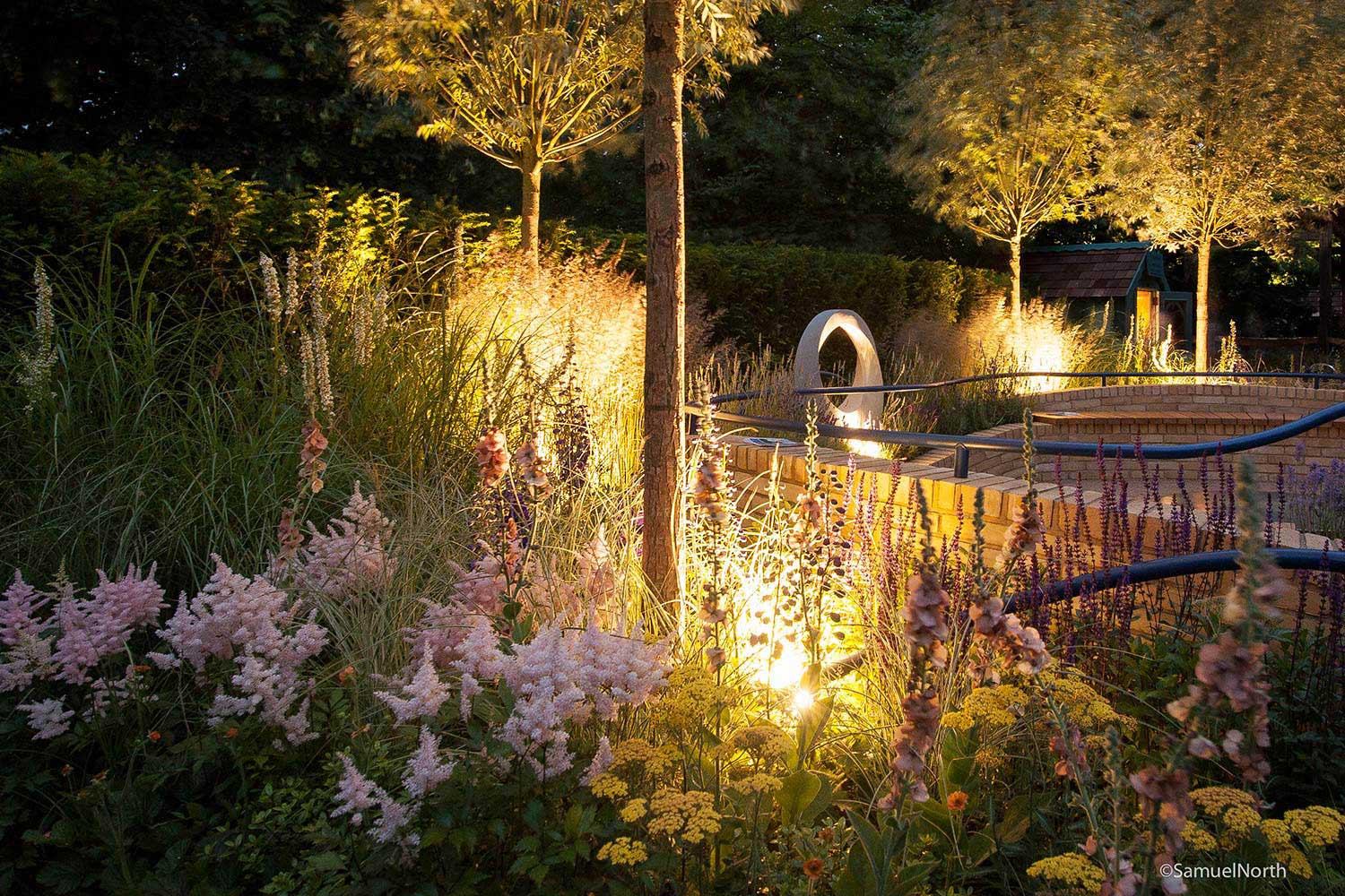 Rae Wilkinson Show Garden with evening lighting. Rae Wilkinson Garden and Landscape Design Surrey, Sussex, Hampshire, London, South-East England